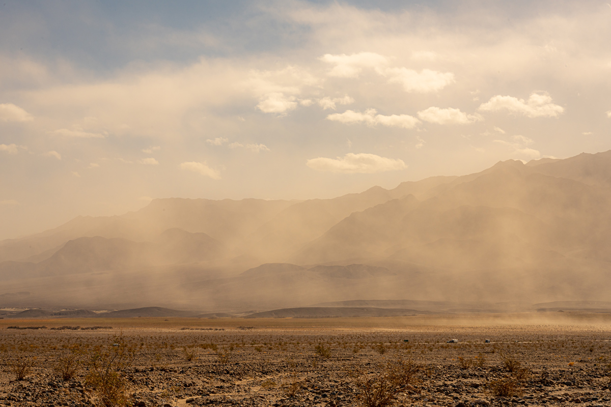 A photo of cars driving on a dusty road in a desert landscape