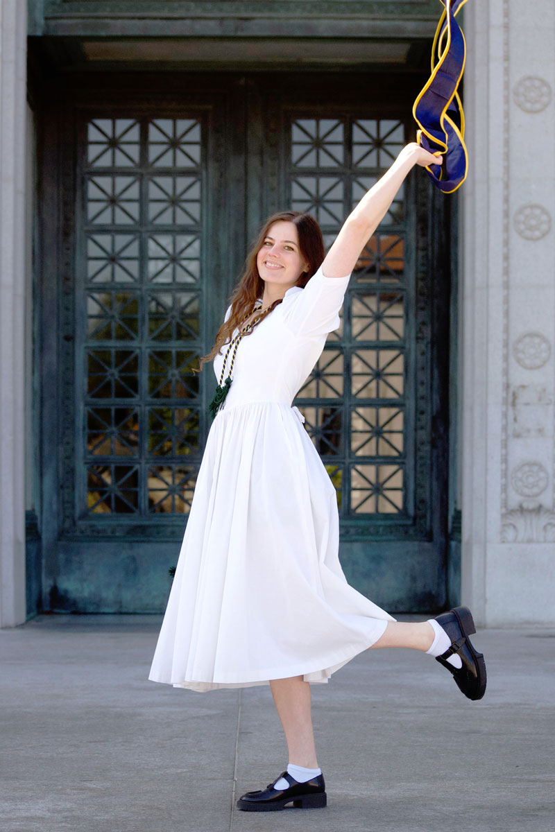 Charlie Kortleven holding up her graduation stole in front of Doe Library