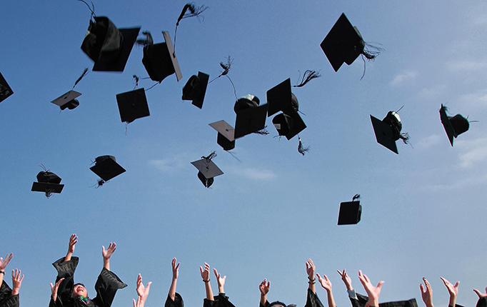 Stock image of group of graduates tossing graduation caps into air