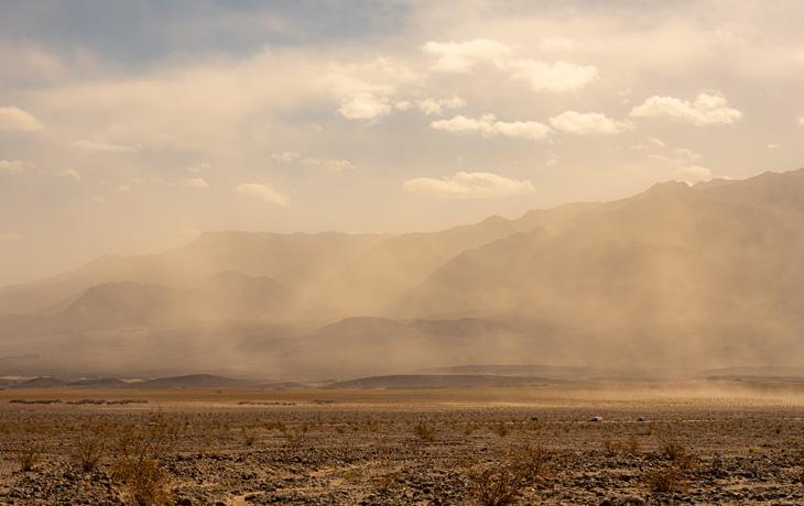 A photo of cars driving on a dusty road in a desert landscape