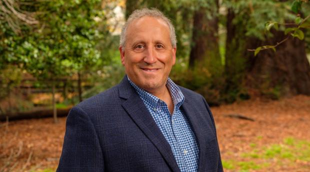 A photo of Professor Allen Goldstein smiling at the camera against a wooded backdrop.