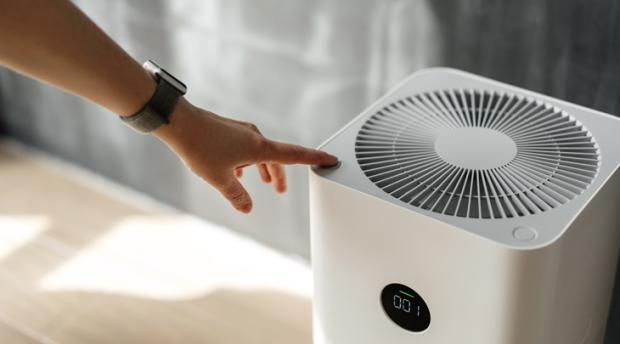 A photo of a person's hand turning on a white air purifier.