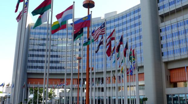 An exterior photo of the United Nations building in Vienna, with several flags representing member nations visible.