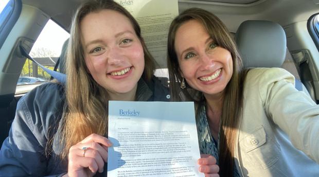 A photo of two women holding up a letter in a car.