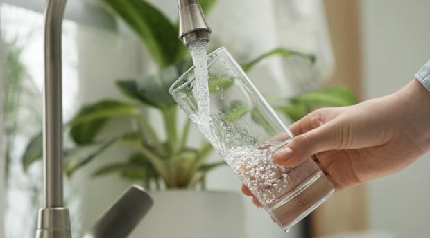 A close-up photo of a person filling glass with water from tap at home.
