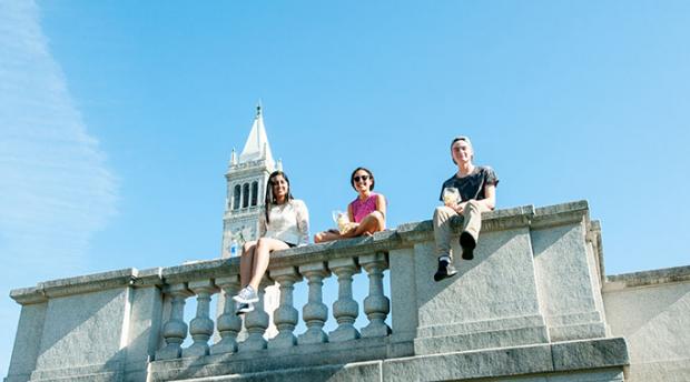 Three students sitting on railing near campanile 