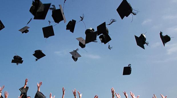 Stock image of group of graduates tossing graduation caps into air